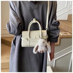 Chic cream-colored small crossbody bag with a cute plush bunny charm shown on stairs