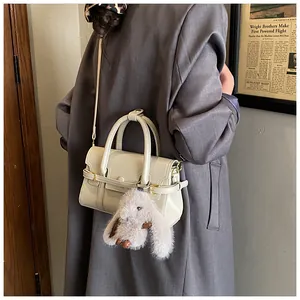 Detail of a beige minimalist handbag with a plush bunny charm and crossbody strap