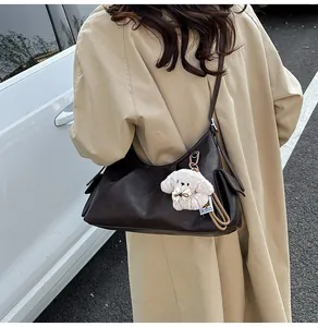 Detail view of a vintage dark brown leather shoulder bag with a cute white dog plush charm