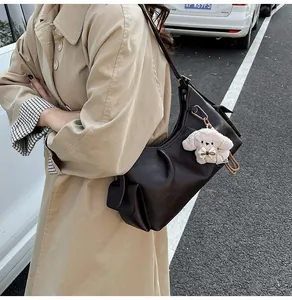 Detail of dark brown pleated hobo bag with beige plush puppy charm and side pocket