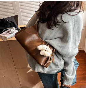 Detail view of a vintage brown leather tote bag with a cute white plush dog charm