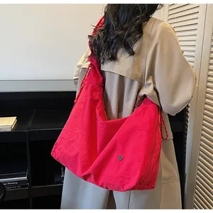 Detail view of a large red pleated tote bag with side zippers on a beige trench coat