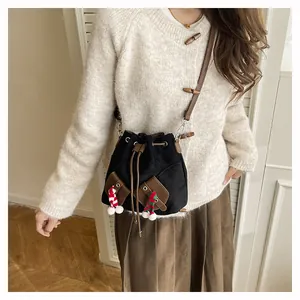Détail d'un sac seau noir à cordon avec poches marron et pompons festifs en fourrure
