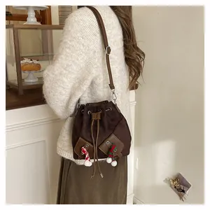 Détail d'un sac seau en daim marron avec pompons festifs et bandoulière en cuir