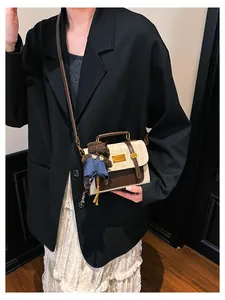 Detail of retro color-block handbag with brown leather trim and a cute teddy bear charm