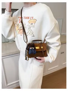 Detail of dark brown matte crossbody bag with gold twist lock and plush bear charm