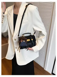 Detail of black leather crossbody bag with gold hardware and brown bear charm on white blazer