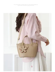 Detail of beige bucket bag with lychee texture leather and floral charm on a shoulder strap