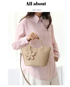 Detail of lychee textured beige bucket bag with flower charm held by model in pink