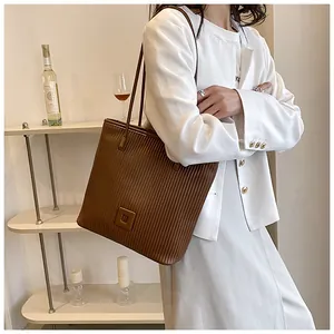 Detail of dark brown tote bag featuring vertical pleat texture and minimalist square logo