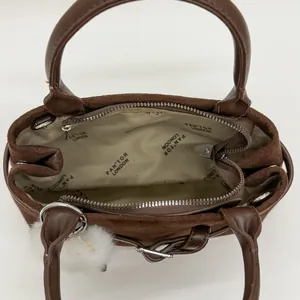 Detail einer braunen Wildleder-Tragetasche mit Marken-Innenfutter und weißem Plüsch-Anhänger