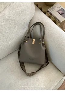 Detail of taupe leather bucket bag with gold hardware and stylish retro patterned strap