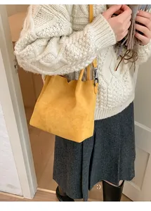 Détail du sac seau en daim jaune moutarde porté par un mannequin en pull d'hiver chaud