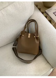 Detail of brown leather bucket bag with gold clasp and geometric pattern wide strap