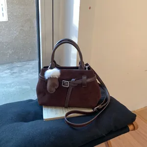 Detail der kaffeebraunen Wildledertasche mit Lederriemen und Handschuhanhänger auf Kissen