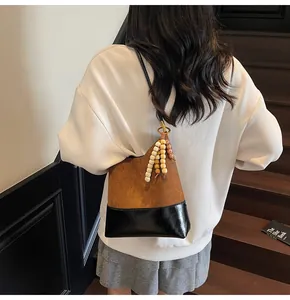 Detail of a brown and black tote bag with wooden bead pendants shown on a model's shoulder
