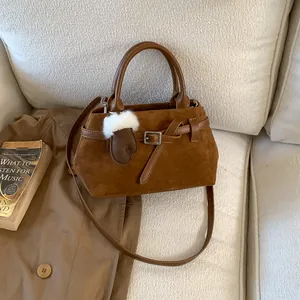 Braune Wildleder-Einkaufstasche mit Griffen und Schultergurt auf einem gemütlichen Sofa
