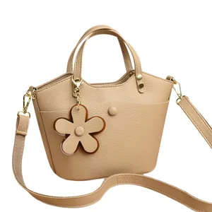 Chic beige lychee leather bucket bag with wave opening and floral charm on white background