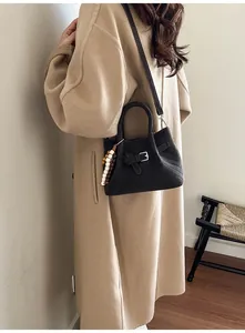 Detail of black suede bag with V-quilted stitching and wooden bead charm on beige coat