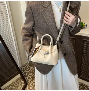 Close-up of cream white handbag with V-shaped embossing and wooden bead pendant