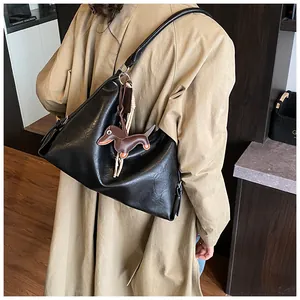 Détail d'un sac hobo en cuir noir avec breloque chien sur un trench-coat classique