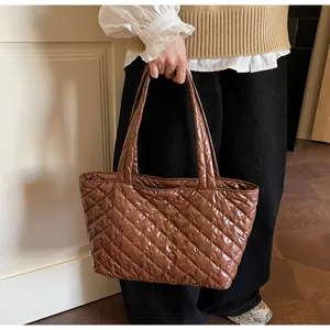 Detail of dark brown quilted tote bag in glossy finish held by a model in casual setting