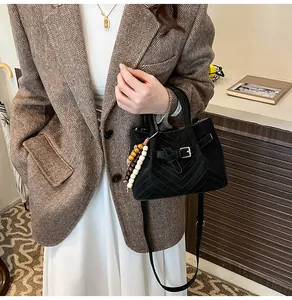 Detail shot of black faux suede crossbody bag with V-quilting and wooden bead charm
