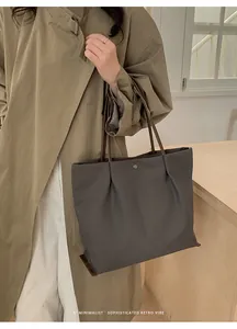 Detail of dark gray tote bag with brown handles and elegant pleated opening design