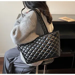 Detail of a large black quilted tote bag with a glossy finish and padded texture