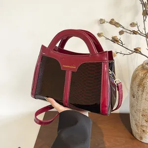 Detail of dark red faux leather handbag with snakeskin texture and gold lettering