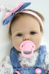 Close-up of realistic baby doll with blue eyes, pink pacifier, and denim overalls