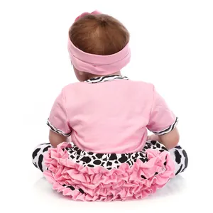 Back view of a lifelike reborn baby doll in pink top and cow-print layered skirt