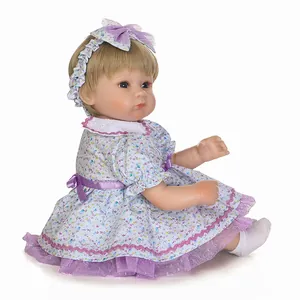 Bambola Reborn realistica con capelli biondi e vestito floreale viola su sfondo bianco