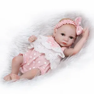 Realistic mini baby doll in pink polka dot outfit on white plush background