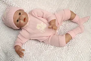 Détail d'une poupée reborn en tenue tricotée rose avec écusson ours sur tapis blanc