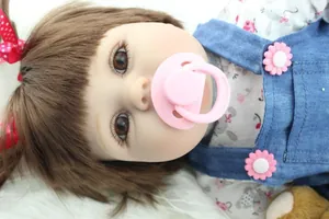 Close-up of lifelike reborn baby doll with brown hair, pink pacifier and denim outfit