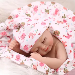 Realistic newborn baby doll in pink floral swaddle and hat on soft plush white rug