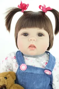 Close-up of lifelike baby doll with brown pigtails and a plush mini teddy bear