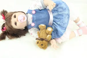 Close-up of realistic reborn doll in blue denim dress with pacifier and teddy bear