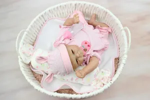 Realistic reborn doll in striped pink outfit resting in a white woven basket with a baby bottle