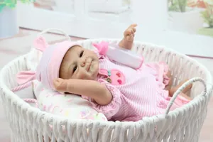 Close-up of lifelike baby doll in pink rabbit outfit with feeding bottle in a woven basket