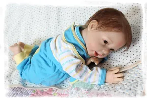 Close-up of lifelike reborn doll wearing blue and yellow striped outfit on soft bedding