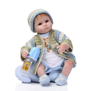 Realistic reborn baby doll in blue knitted cardigan with nursing bottle on white background