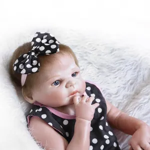 Realistic reborn baby doll in polka dot outfit laying on soft white plush rug
