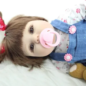 Realistic reborn baby doll girl with brown hair in blue denim overalls and floral shirt