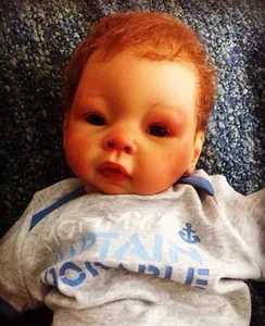 Close-up of realistic newborn baby doll face with brown hair and anchor print onesie