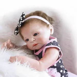 Realistic reborn baby doll in pink polka dot dress on white soft plush background