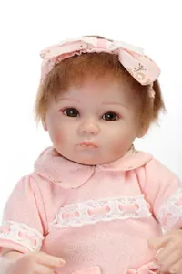Close-up of a lifelike baby doll with pink knit dress and floral bow headband