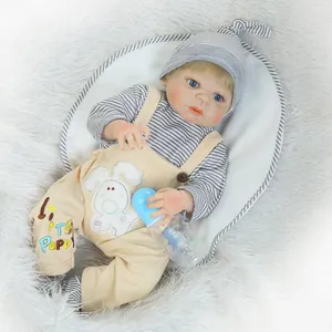 Lifelike reborn baby doll in khaki overalls with blue bottle on white faux fur background