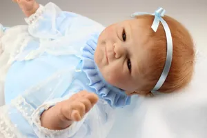 Détail de la poupée reborn avec peau réaliste, cheveux bruns et tenue en dentelle bleue